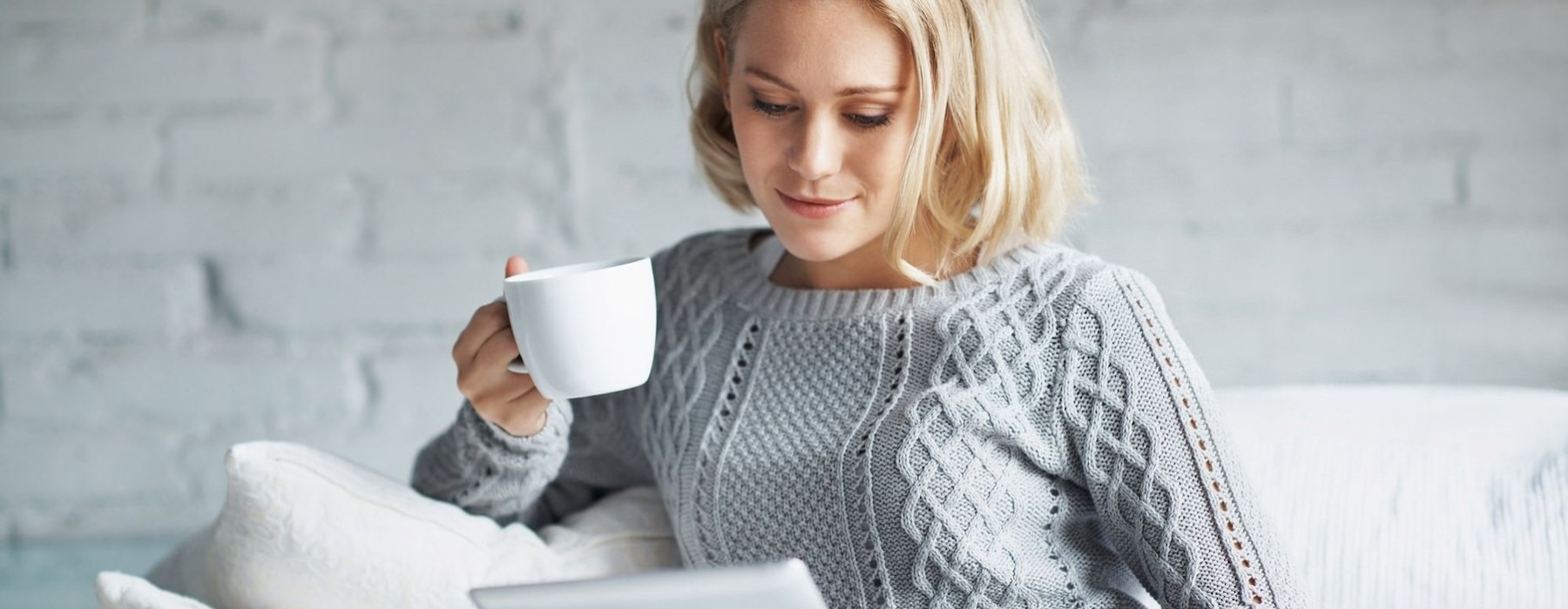 a woman holding a coffee cup looking at a tablet
